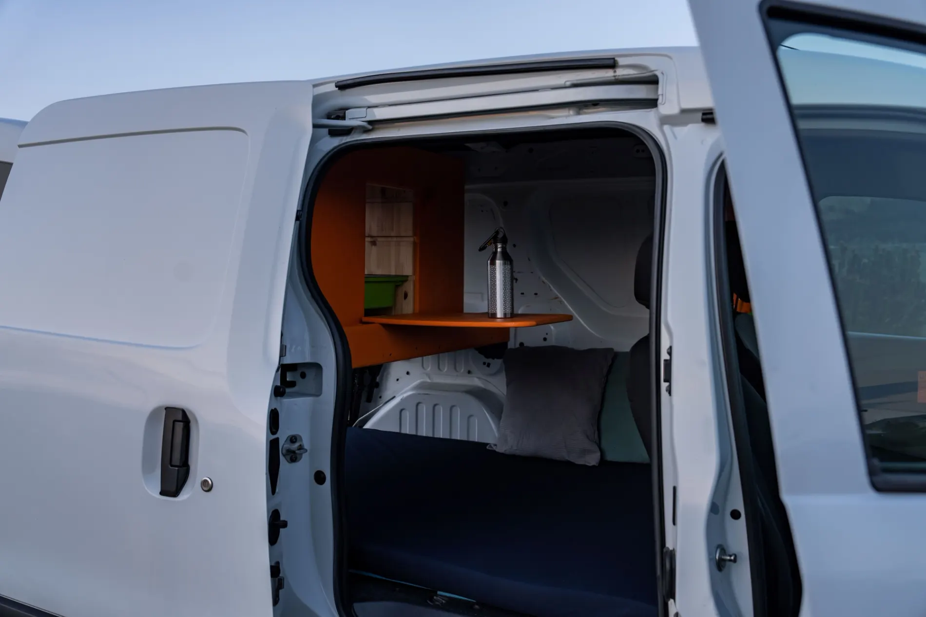 Inside a Go Campers campervan showing the bed, fold-out table and storage shelf